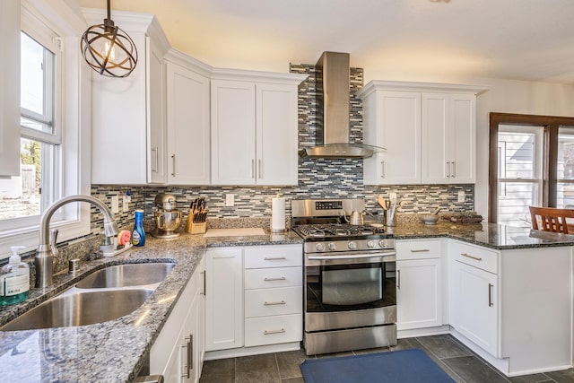 kitchen featuring stainless steel gas stove, a sink, a peninsula, white cabinets, and wall chimney range hood