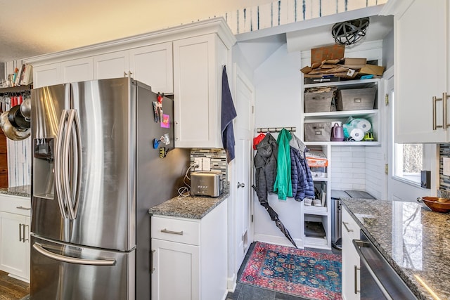 kitchen featuring tasteful backsplash, stainless steel fridge, white cabinetry, and dark stone countertops