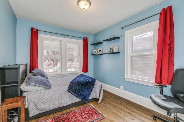 bedroom featuring wood finished floors, baseboards, and a textured ceiling