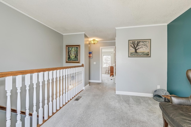 hallway with visible vents, a textured ceiling, carpet floors, crown molding, and baseboards