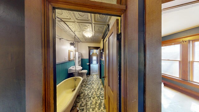 full bath featuring a bath, a wainscoted wall, toilet, and an ornate ceiling