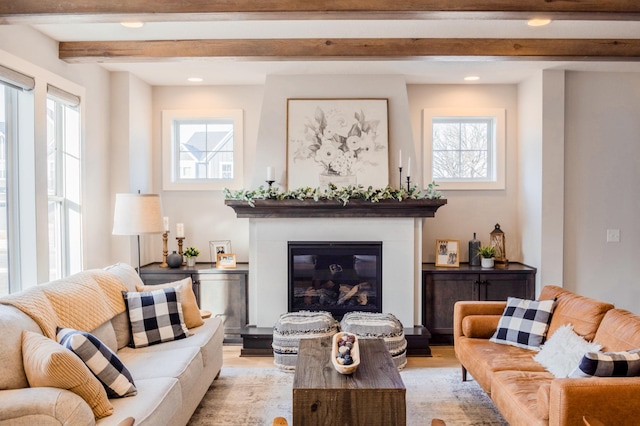 living area with recessed lighting, a glass covered fireplace, a healthy amount of sunlight, and beamed ceiling