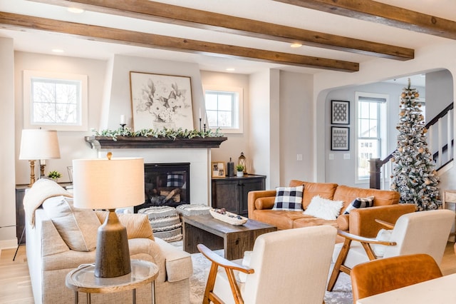 living room featuring stairway, beam ceiling, recessed lighting, light wood-style floors, and a glass covered fireplace