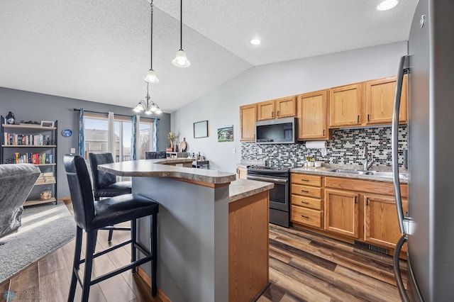 kitchen with a sink, stainless steel appliances, vaulted ceiling, dark wood-type flooring, and a center island