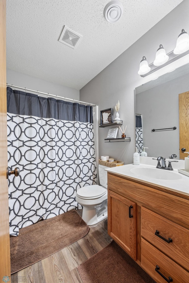 bathroom featuring toilet, wood finished floors, visible vents, and a textured ceiling