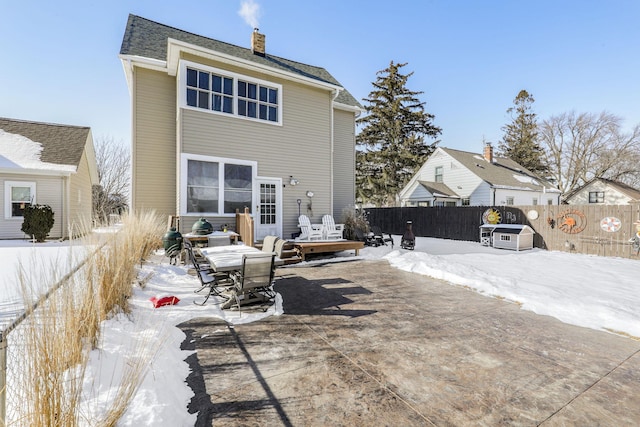 snow covered rear of property with a patio area, a chimney, and fence