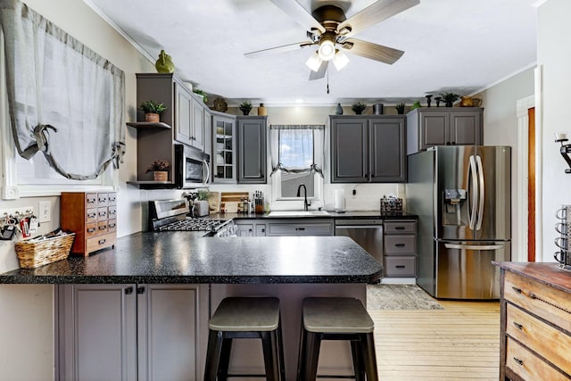 kitchen with dark countertops, ornamental molding, appliances with stainless steel finishes, a peninsula, and a sink