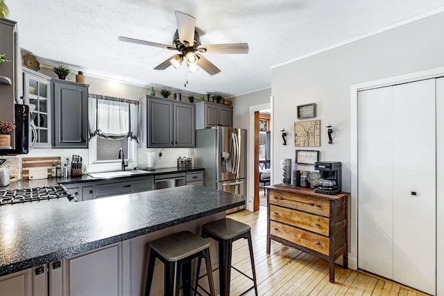 kitchen featuring light wood finished floors, crown molding, appliances with stainless steel finishes, a peninsula, and a sink