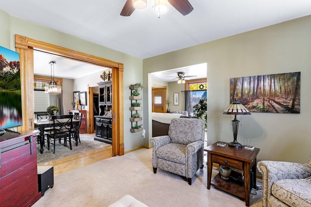 living area featuring baseboards, light colored carpet, and ceiling fan with notable chandelier