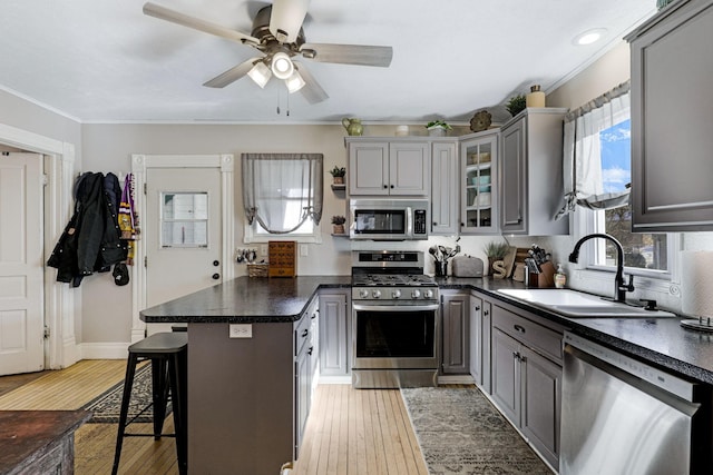 kitchen featuring a peninsula, gray cabinets, a sink, stainless steel appliances, and dark countertops