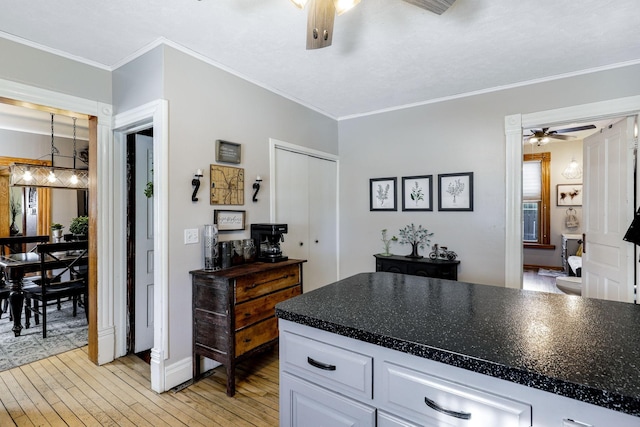 kitchen with light wood finished floors, dark countertops, crown molding, ceiling fan, and white cabinets