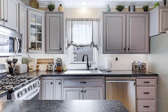 kitchen with a sink, stainless steel appliances, glass insert cabinets, and dark countertops