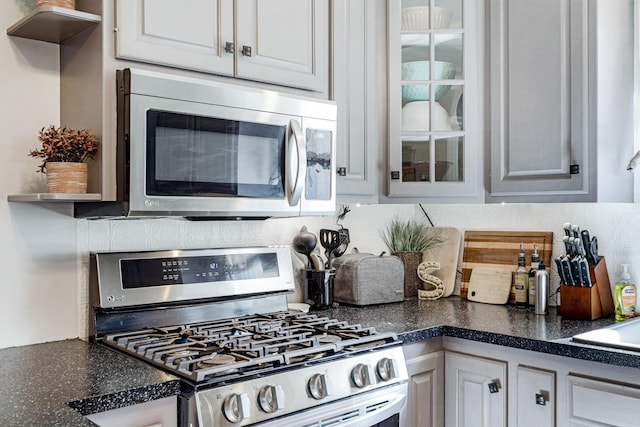 kitchen featuring tasteful backsplash, glass insert cabinets, stainless steel appliances, and dark countertops