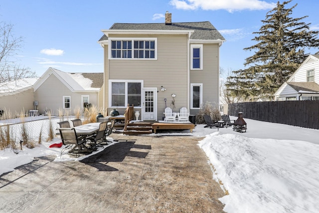 snow covered back of property with a deck, a chimney, outdoor dining area, and a fenced backyard