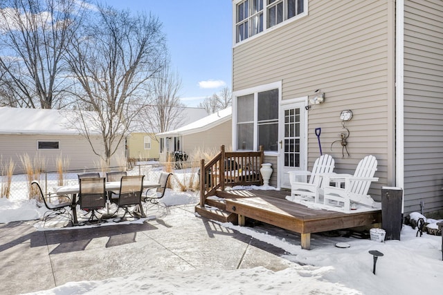 snow covered patio with outdoor dining space, fence, and a wooden deck