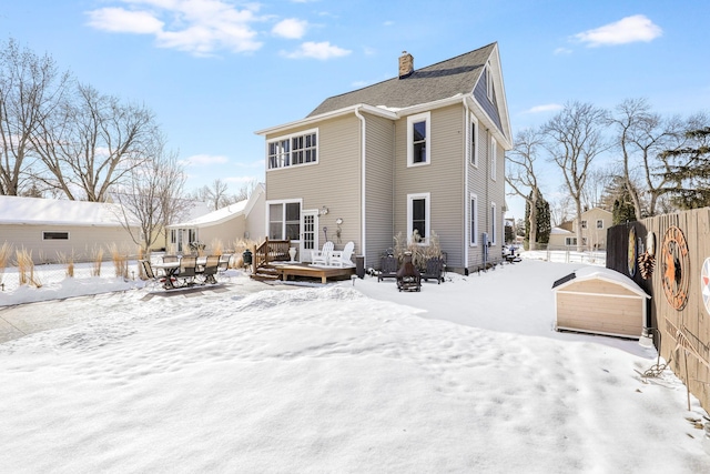 snow covered rear of property with a deck, a chimney, and fence