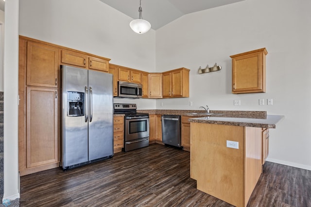 kitchen featuring dark countertops, dark wood-type flooring, a peninsula, stainless steel appliances, and a sink