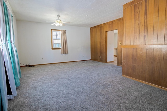 empty room featuring wooden walls, a ceiling fan, and carpet floors