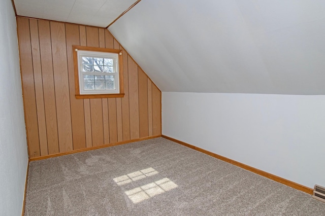 additional living space featuring baseboards, wooden walls, carpet flooring, and vaulted ceiling