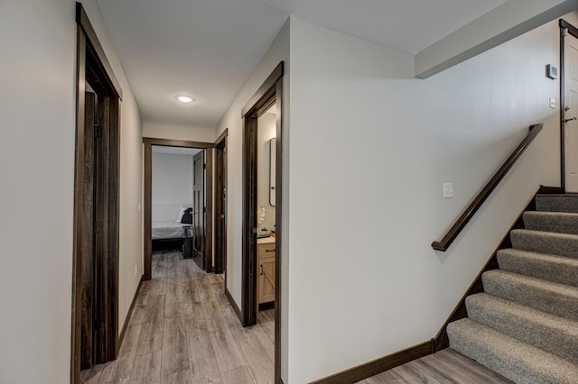 corridor featuring stairway, baseboards, and light wood finished floors