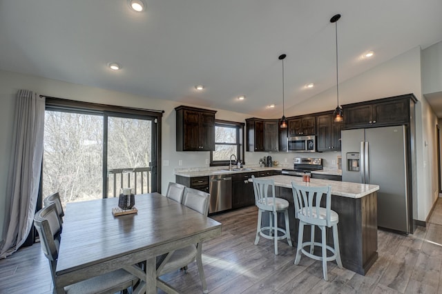 kitchen featuring vaulted ceiling, a center island, light wood finished floors, dark brown cabinets, and appliances with stainless steel finishes