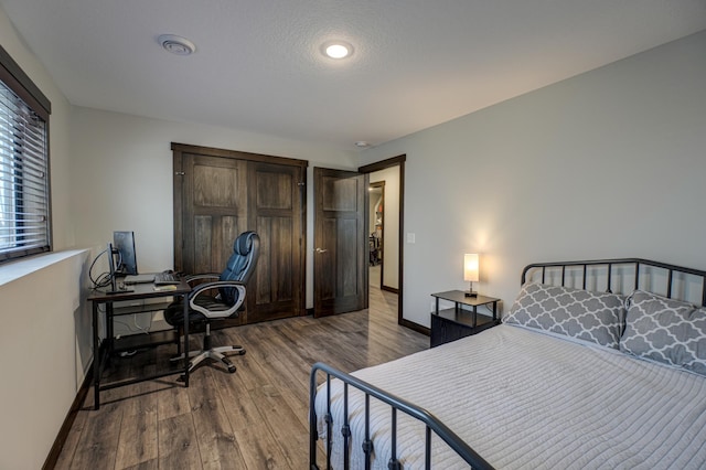 bedroom with visible vents, a textured ceiling, baseboards, and wood finished floors