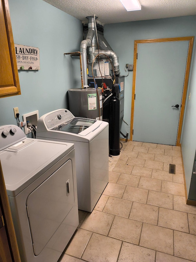 washroom with a textured ceiling, stone tile floors, gas water heater, cabinet space, and washing machine and clothes dryer