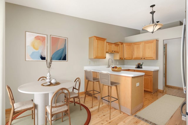 kitchen featuring light countertops, light wood-type flooring, a breakfast bar, a peninsula, and light brown cabinetry