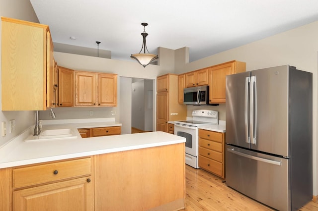 kitchen with light brown cabinets, a sink, stainless steel appliances, light wood-style flooring, and a peninsula