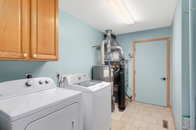 clothes washing area featuring washing machine and clothes dryer, a textured ceiling, water heater, cabinet space, and visible vents