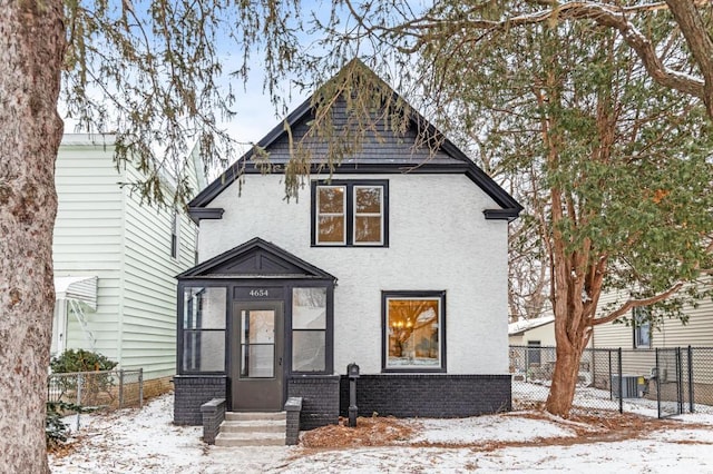 view of front of house featuring brick siding, fence, entry steps, stucco siding, and a sunroom