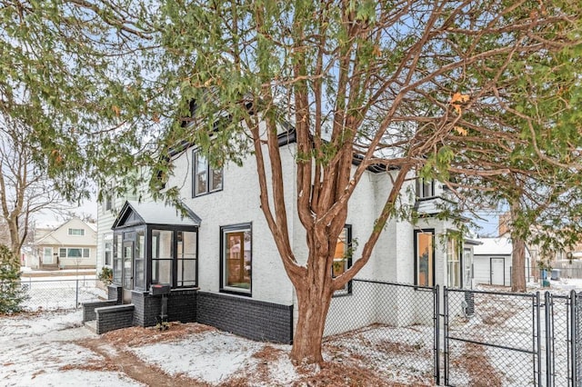 view of snowy exterior featuring brick siding, fence private yard, stucco siding, a sunroom, and a gate