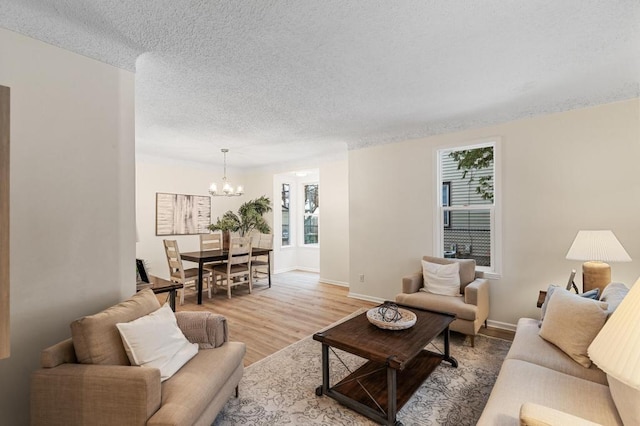 living room featuring baseboards, a textured ceiling, a chandelier, and light wood finished floors