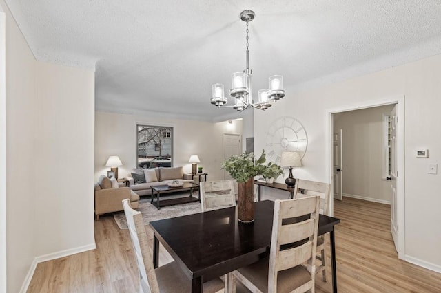 dining area featuring a notable chandelier, baseboards, light wood-type flooring, and a textured ceiling