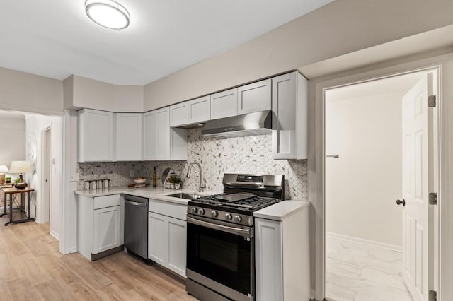 kitchen with under cabinet range hood, light countertops, decorative backsplash, appliances with stainless steel finishes, and a sink