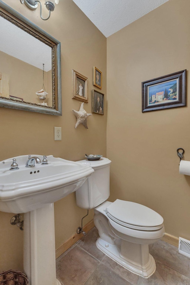 half bathroom with toilet, tile patterned floors, a textured ceiling, baseboards, and visible vents