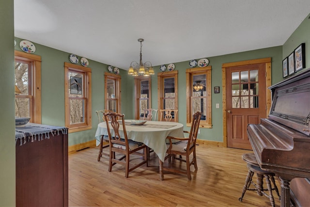 dining space with baseboards, light wood-style floors, and a notable chandelier