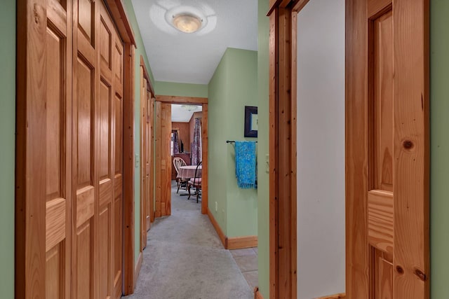 hall with baseboards and light colored carpet