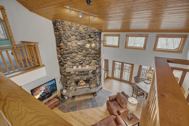 living area with rail lighting, a stone fireplace, wood finished floors, vaulted ceiling, and wood ceiling