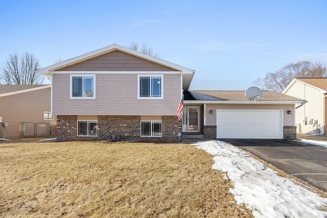 split level home featuring aphalt driveway, an attached garage, brick siding, and a front lawn