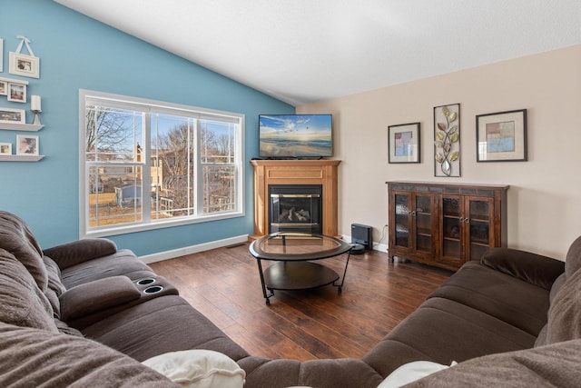 living area featuring a glass covered fireplace, vaulted ceiling, wood finished floors, and baseboards