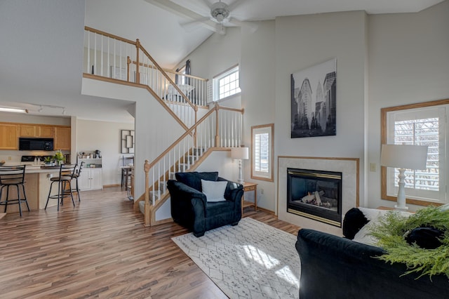 living room featuring stairway, a ceiling fan, light wood-style flooring, a high ceiling, and a tile fireplace