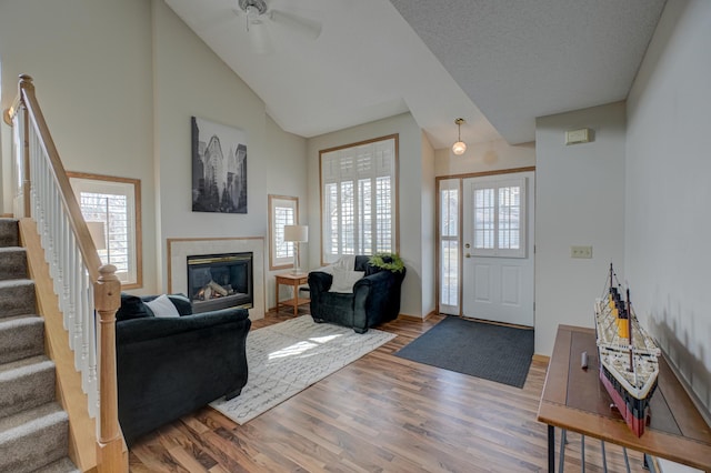 living room with a ceiling fan, wood finished floors, high vaulted ceiling, a fireplace, and stairs