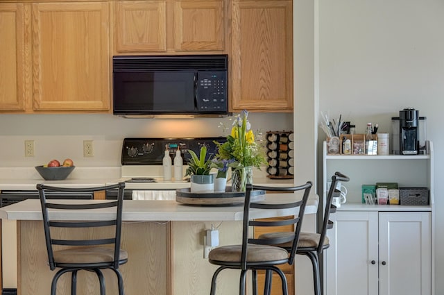 kitchen with white electric range oven, a breakfast bar, black microwave, and light countertops