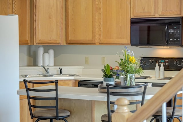 kitchen with a breakfast bar area, freestanding refrigerator, a sink, light countertops, and black microwave