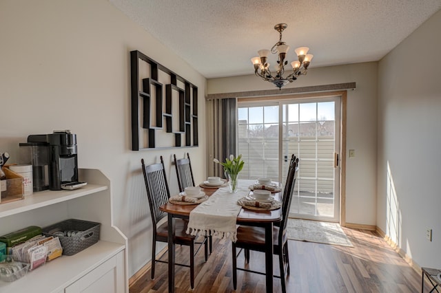 dining space with baseboards, a textured ceiling, an inviting chandelier, and wood finished floors