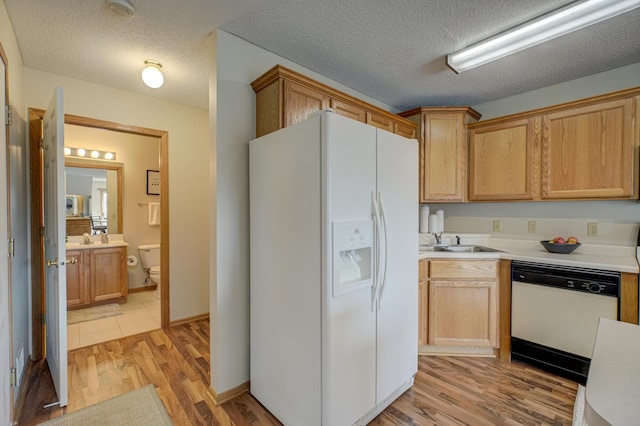 kitchen with white appliances, a sink, light countertops, a textured ceiling, and light wood-type flooring