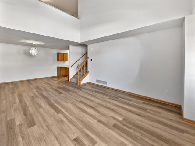 unfurnished living room with stairway, visible vents, baseboards, a high ceiling, and light wood-style floors