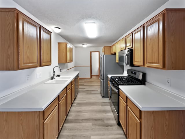 kitchen featuring light wood-style flooring, a sink, a textured ceiling, appliances with stainless steel finishes, and light countertops