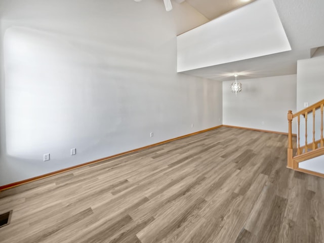 unfurnished living room with baseboards, a notable chandelier, wood finished floors, and stairs